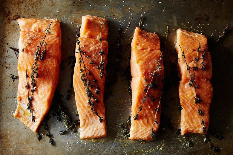 Raw salmon on baking sheet covered in herbs.